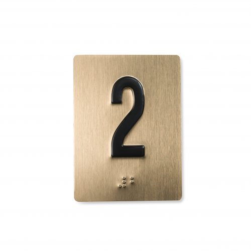Shows an piece of jamb braille in embossed metal with a black character and a satin bronze background